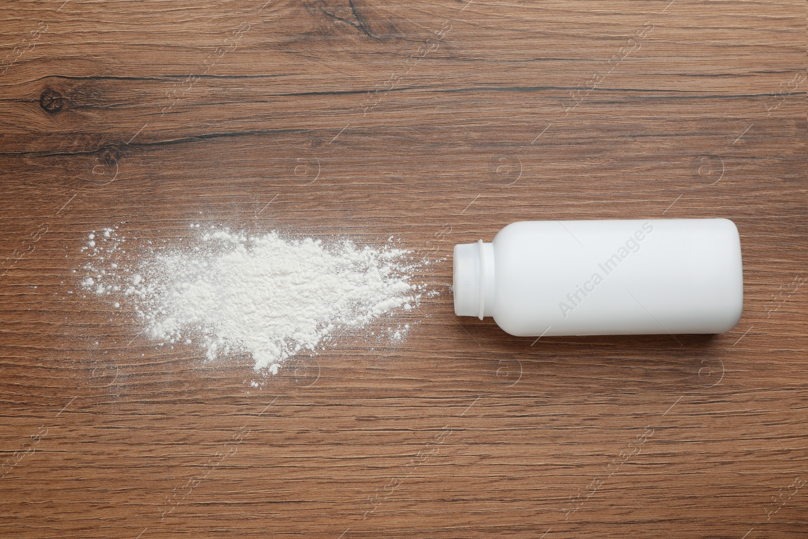 Photo of Bottle and scattered dusting powder on wooden background, top view. Baby cosmetic product