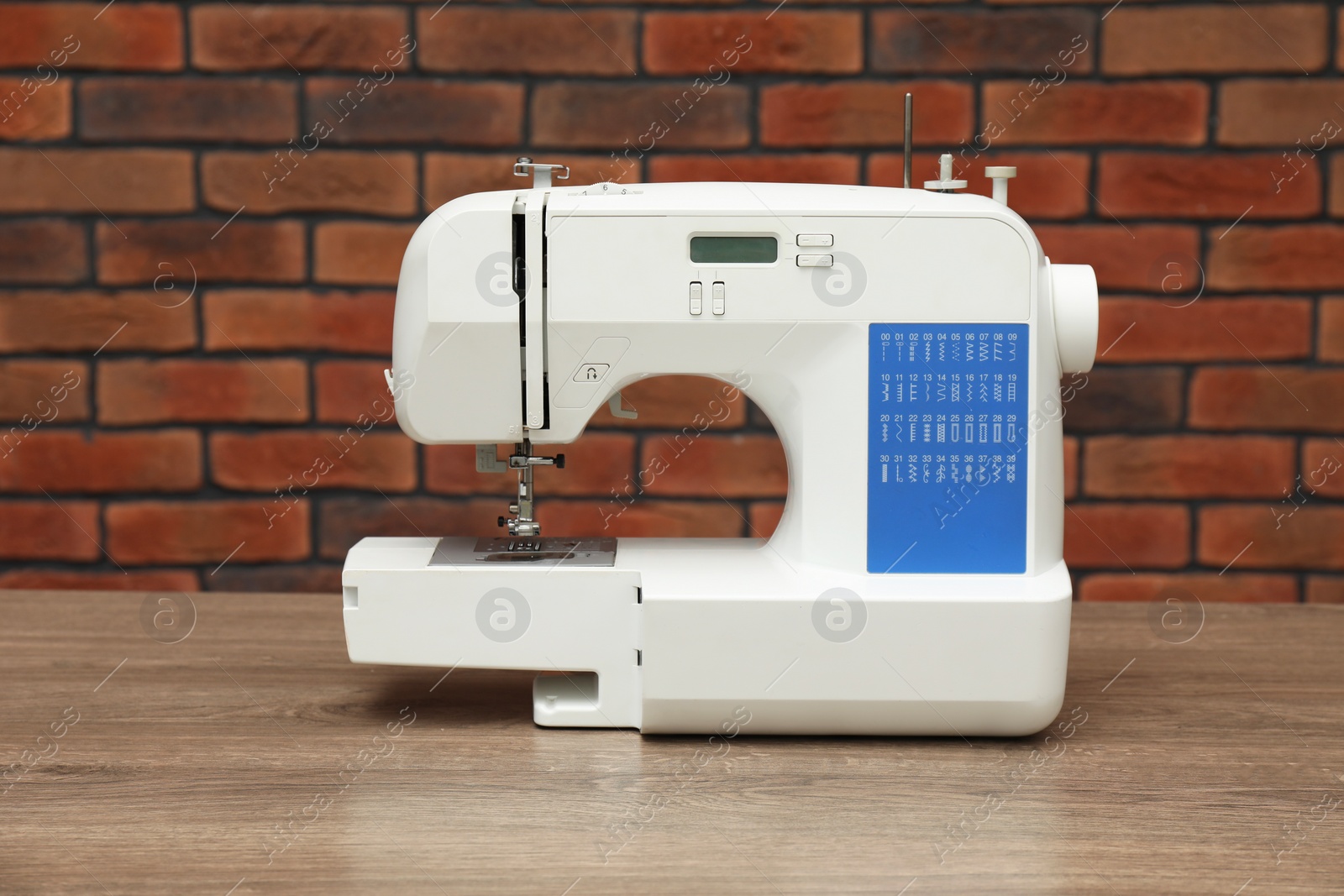 Photo of Sewing machine on wooden table against brick wall