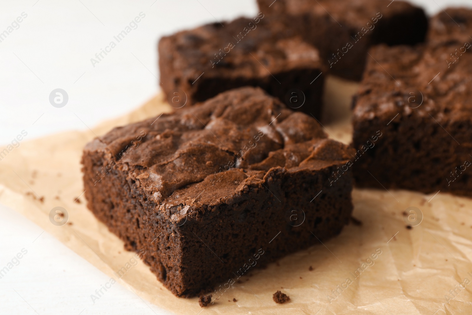 Photo of Parchment paper with fresh brownies on white table, closeup. Delicious chocolate pie