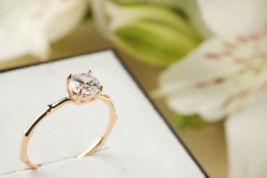 Photo of Beautiful engagement ring in box against blurred background, closeup. Space for text