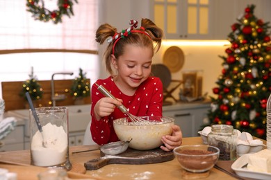 Photo of Cute little girl having fun while making dough for Christmas cookies in kitchen