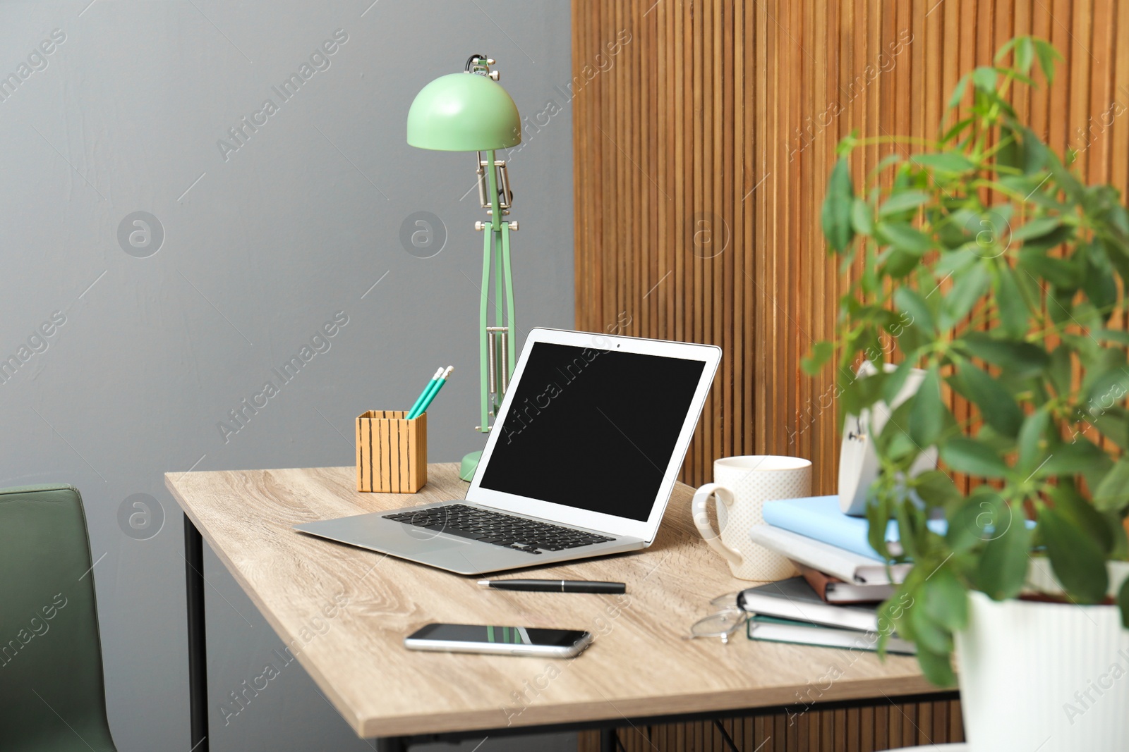 Photo of Stylish workplace interior with laptop on table near wooden wall. Space for text