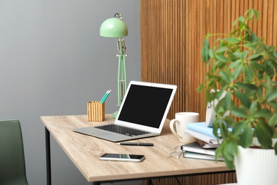 Stylish workplace interior with laptop on table near wooden wall. Space for text