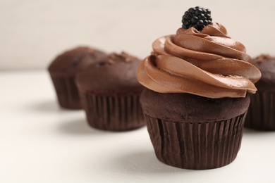 Photo of Delicious chocolate cupcake with cream and blackberry on white table, closeup. Space for text