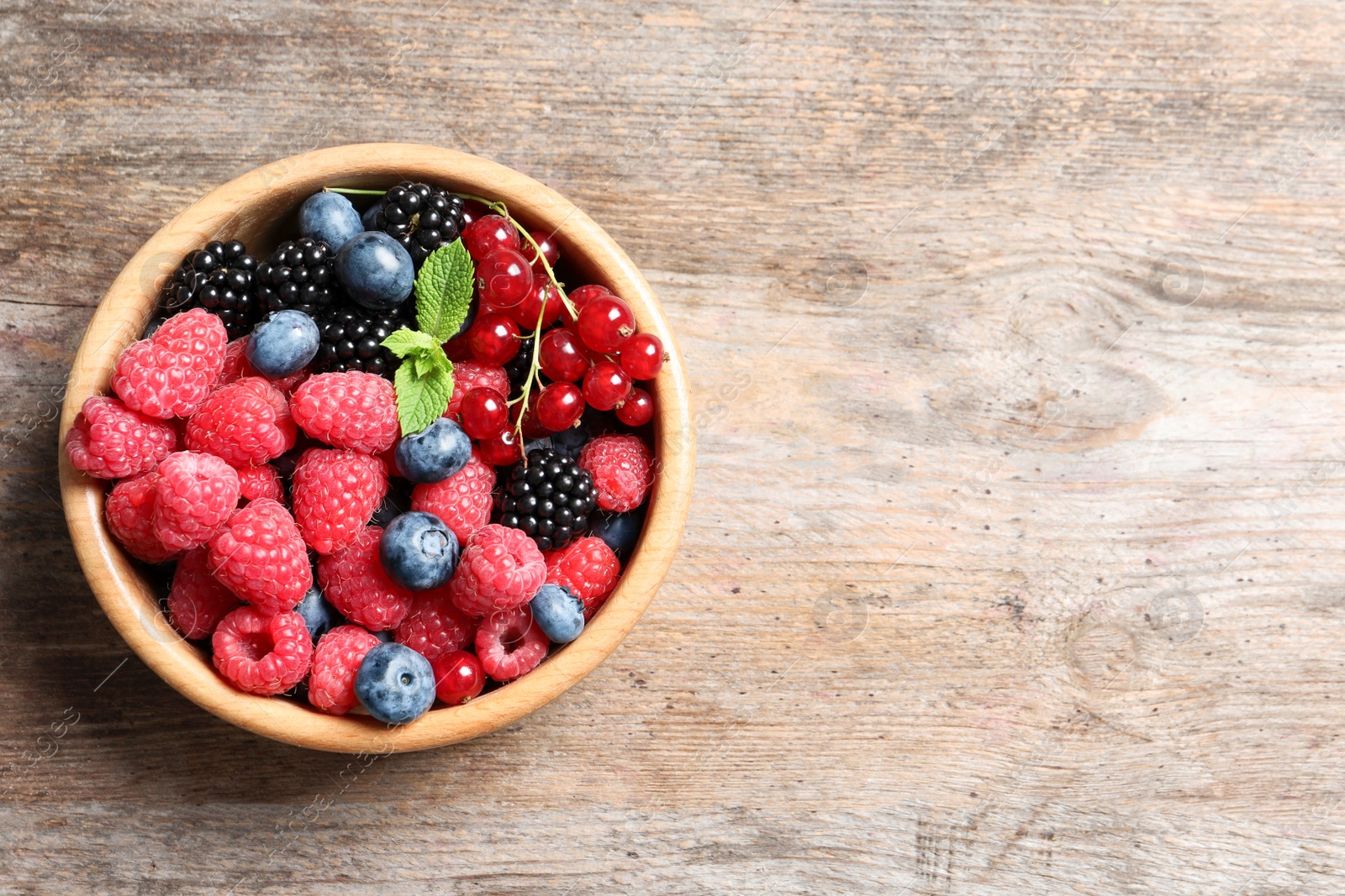 Photo of Bowl with raspberries and different berries on wooden table, top view