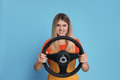Photo of Emotional young woman with steering wheel on light blue background