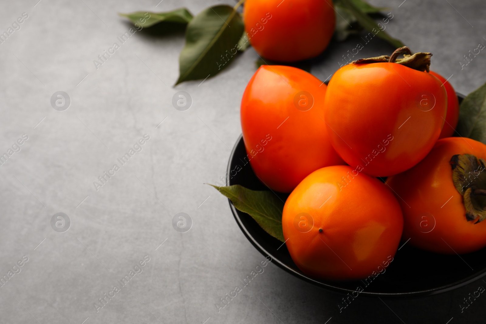 Photo of Delicious ripe persimmons in bowl on light gray table, space for text