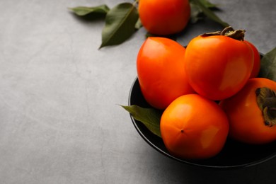 Delicious ripe persimmons in bowl on light gray table, space for text