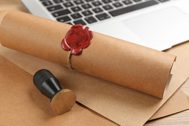 Photo of Notary's public pen and sealed document near laptop on wooden table, closeup