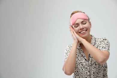 Beautiful woman wearing pajamas and sleeping mask on light grey background, space for text. Bedtime