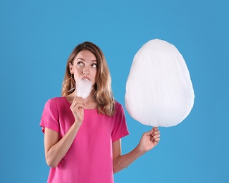 Emotional young woman eating cotton candy on blue background