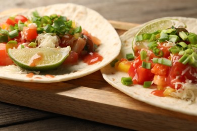 Photo of Delicious tacos with vegetables, green onion, lime and ketchup on wooden table, closeup