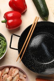 Black wok, chopsticks and products on color table, flat lay