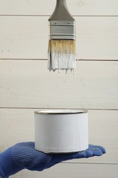 Worker with can of white paint and brush against wooden background, closeup