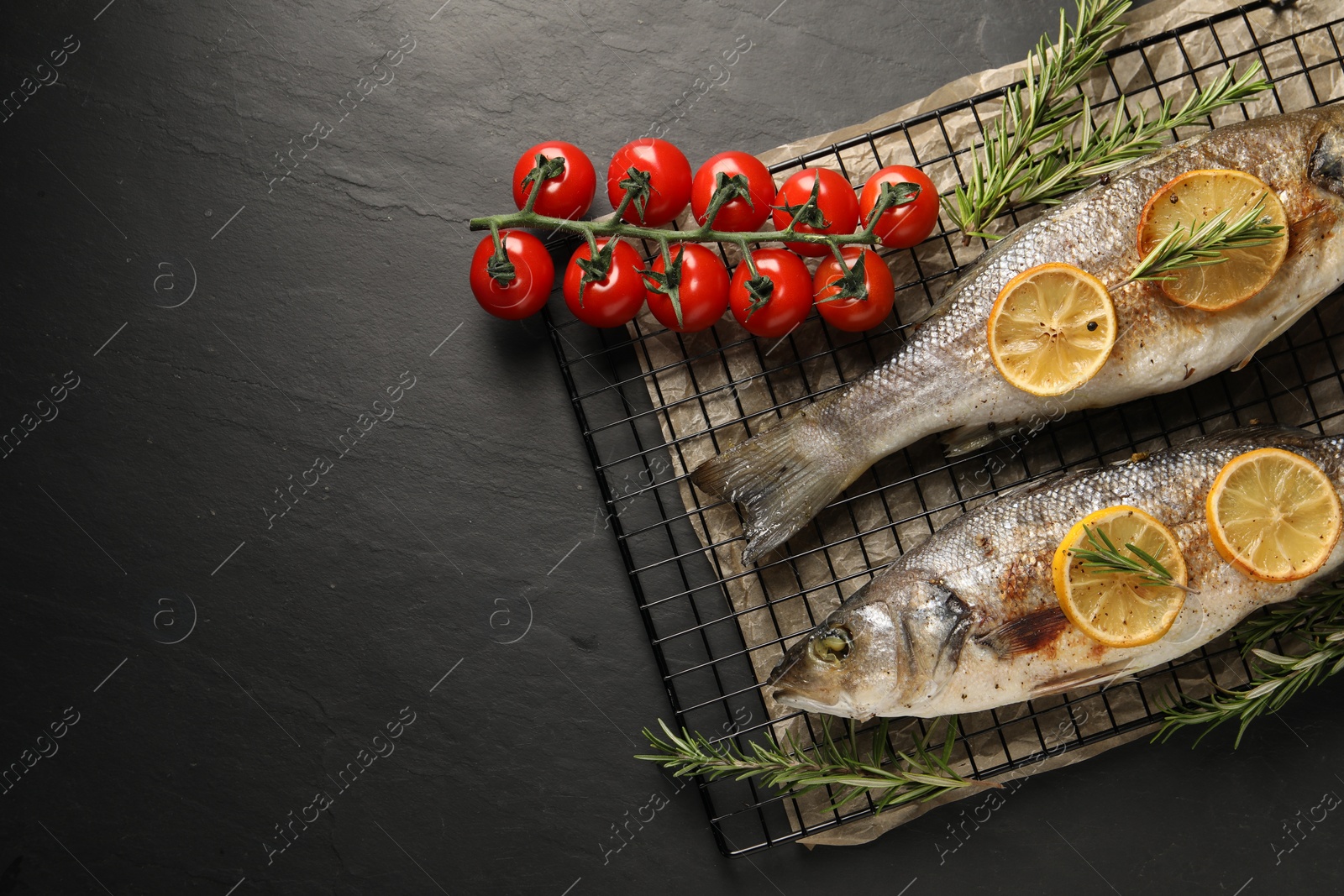 Photo of Baked fish with tomatoes, rosemary and lemon on black textured table, top view. Space for text