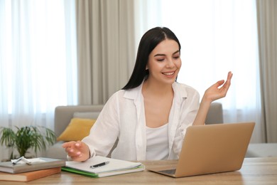 Photo of Young woman watching online webinar at table indoors