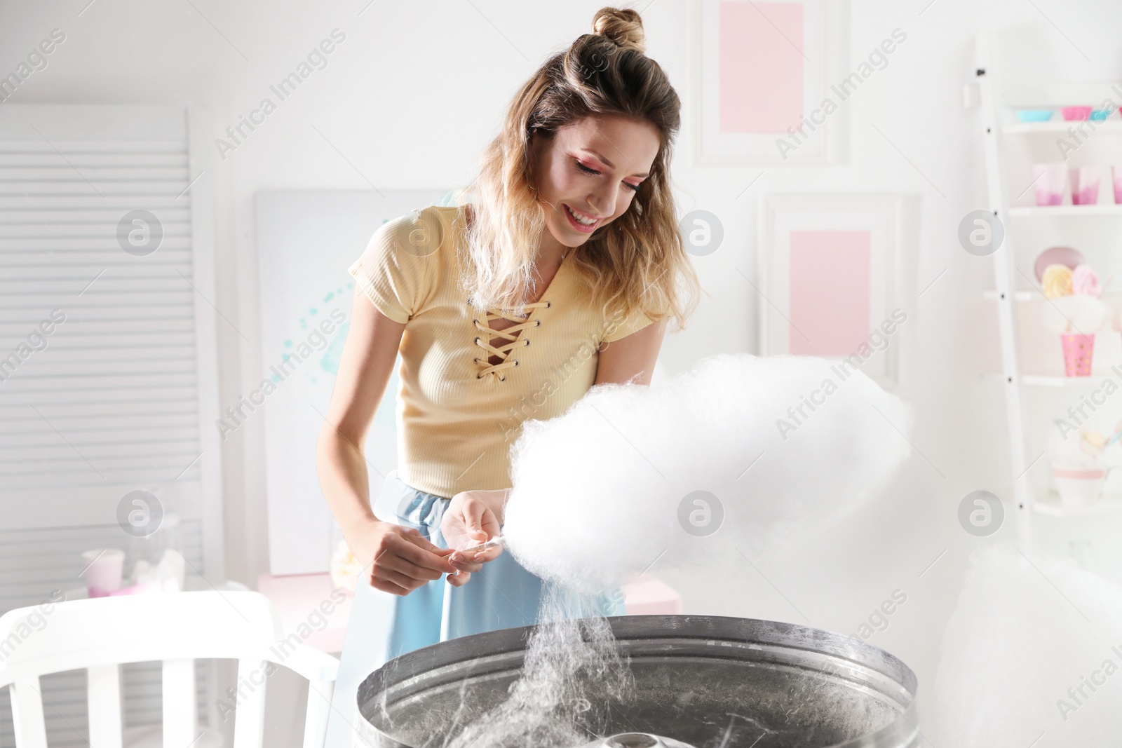 Photo of Young woman making cotton candy using modern machine in room