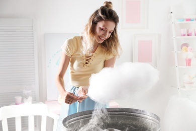 Young woman making cotton candy using modern machine in room