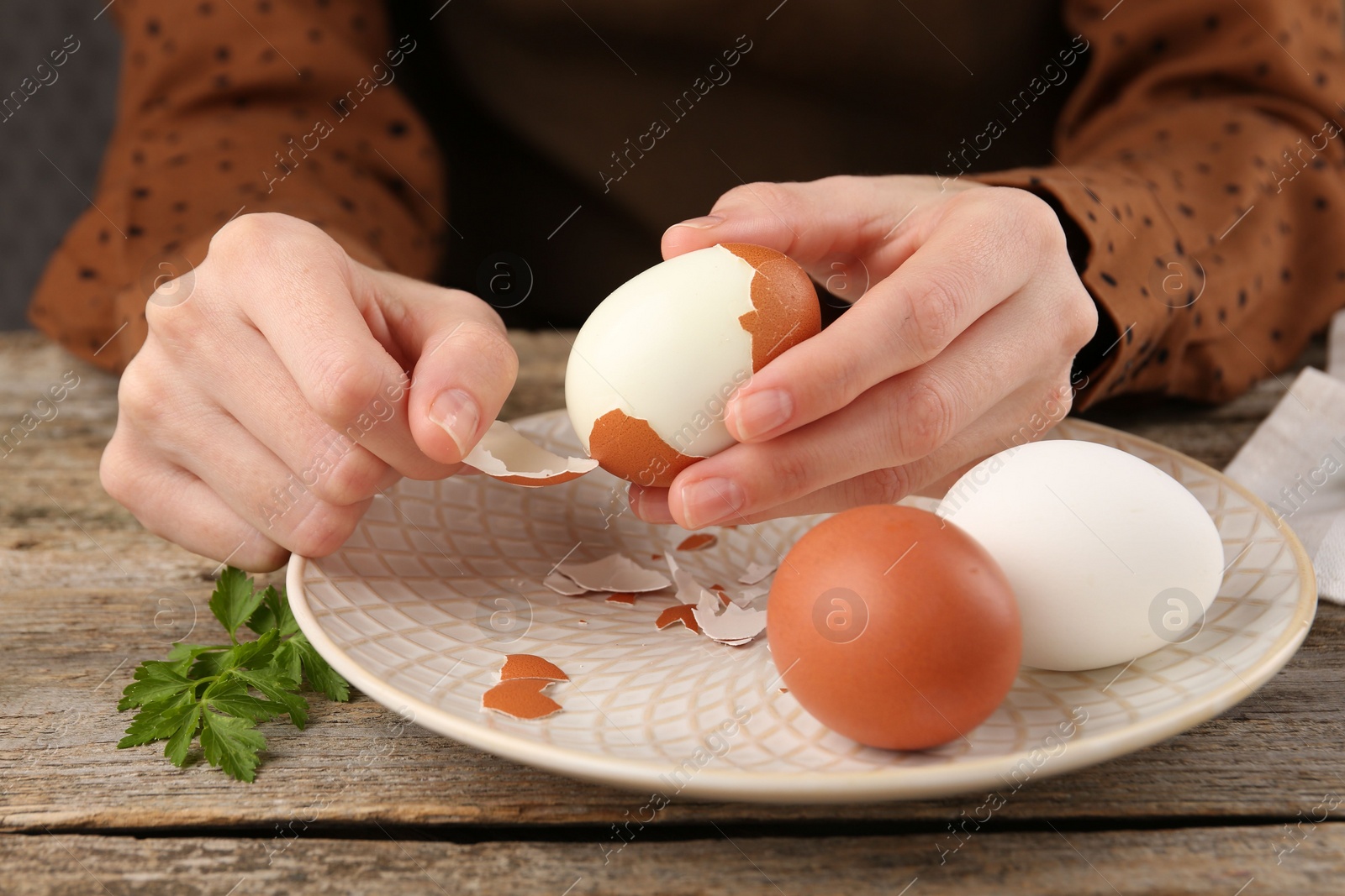 Photo of Woman peeling boiled egg at old wooden table, closeup