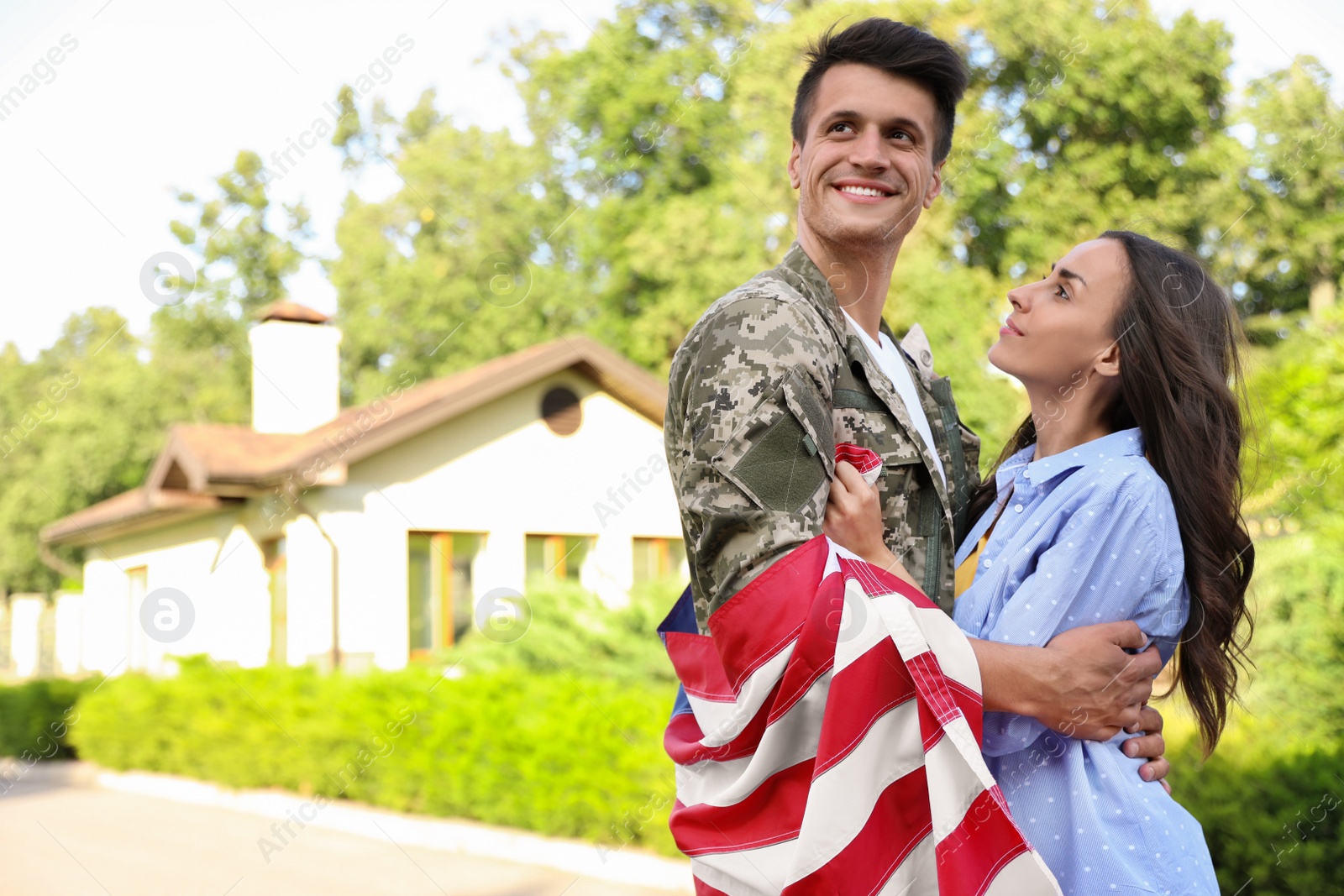 Photo of Man in military uniform with American flag hugging his wife outdoors