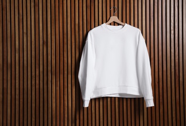 Photo of Hanger with new sweater on wooden wall, mock up for design