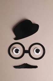 Photo of Man's face made of fake mustache, paper hat and glasses on grey background, top view