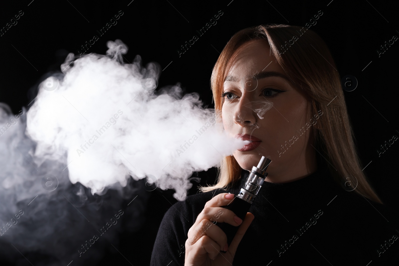 Photo of Young woman using electronic cigarette on black background