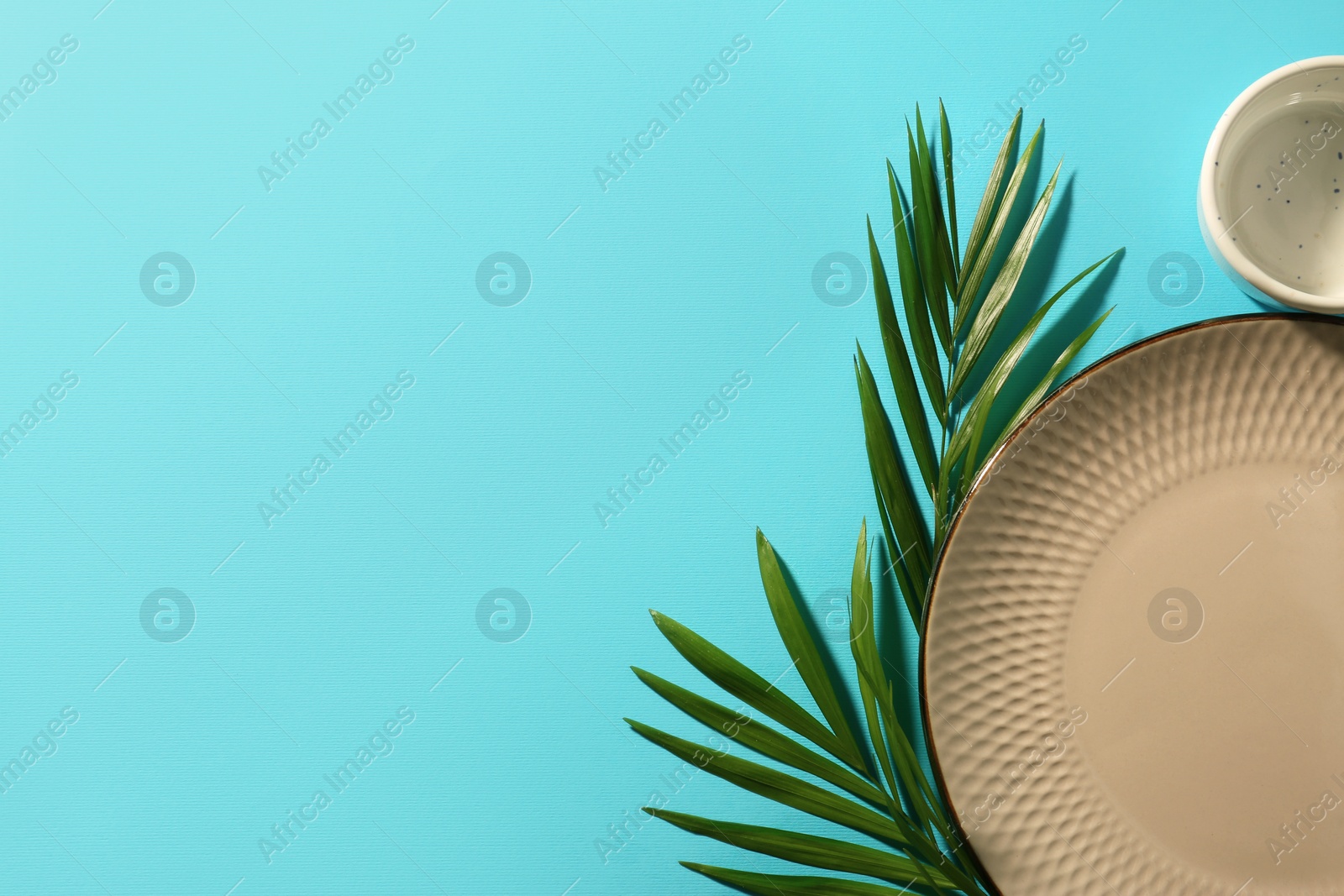 Photo of Ceramic plate, bowl and green leaves on turquoise background, flat lay. Space for text