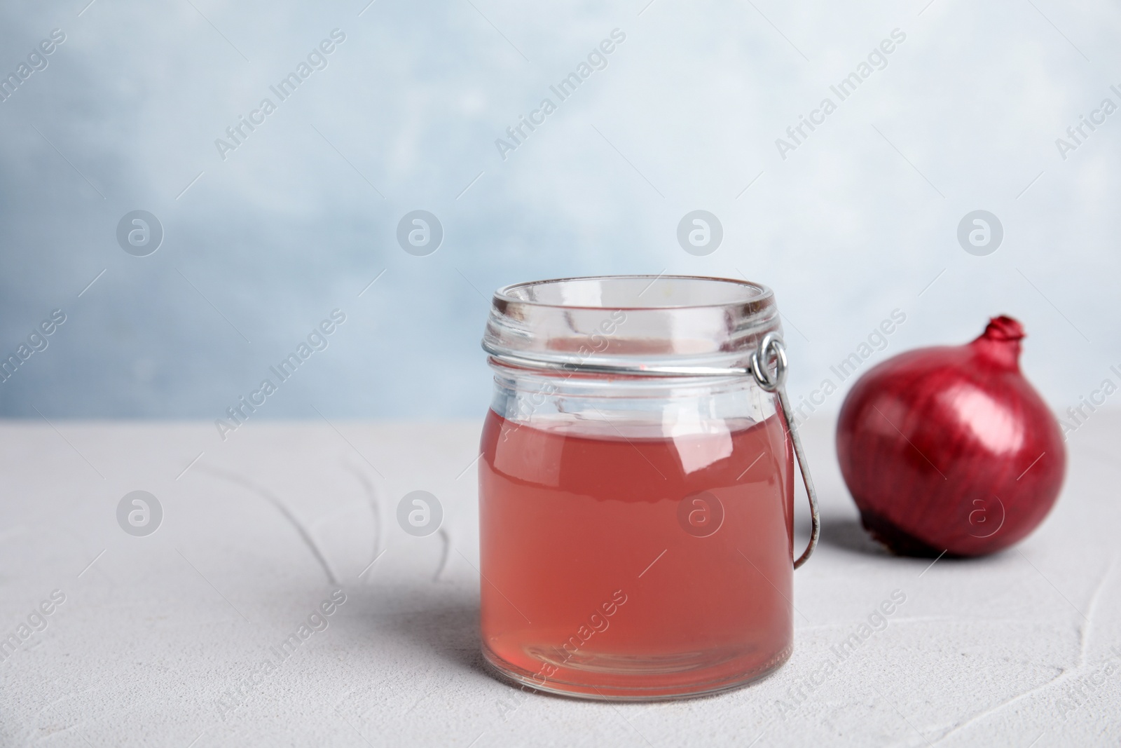 Photo of Glass jar with onion syrup and fresh vegetable on table. Space for text