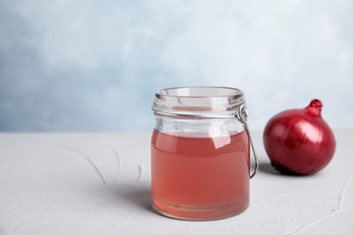 Glass jar with onion syrup and fresh vegetable on table. Space for text