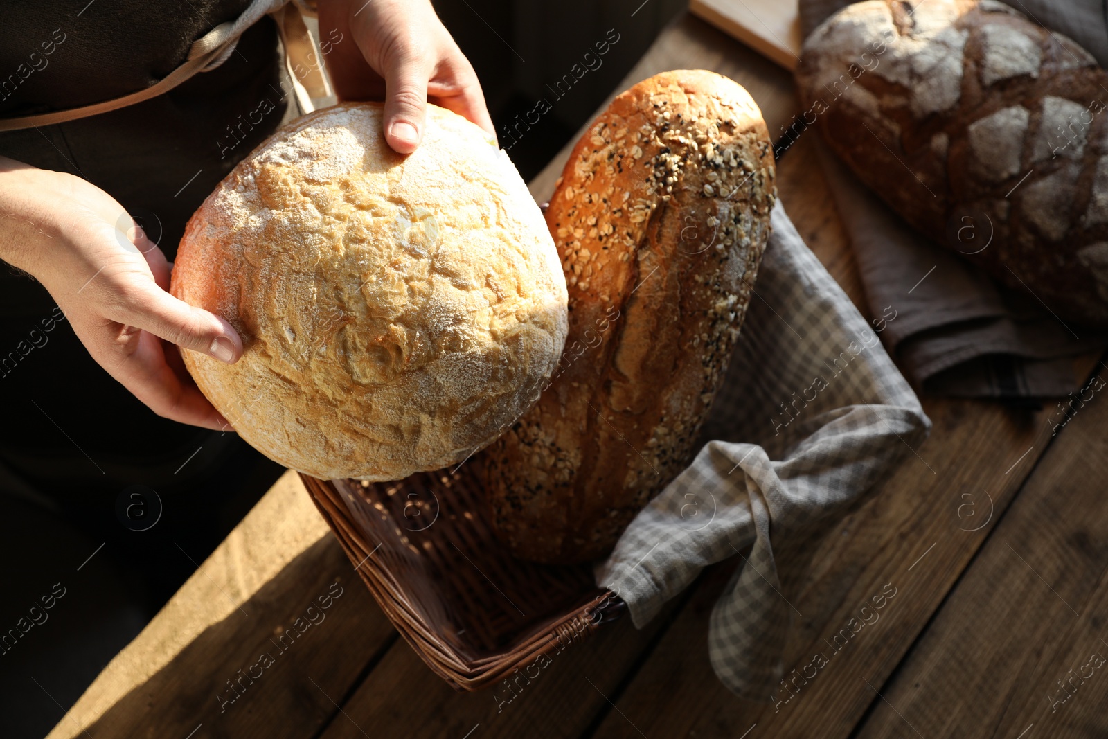 Photo of Man holding wicker basket with different types of bread at wooden table indoors, above view