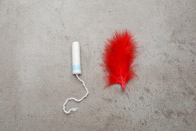 Photo of Tampon and red feather on grey background, flat lay. Menstrual hygiene product