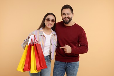 Photo of Happy couple with shopping bags on beige background