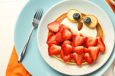 Photo of Creative serving for kids. Plate with cute owl made of pancakes, strawberries, cream, banana and almond on white wooden table, top view