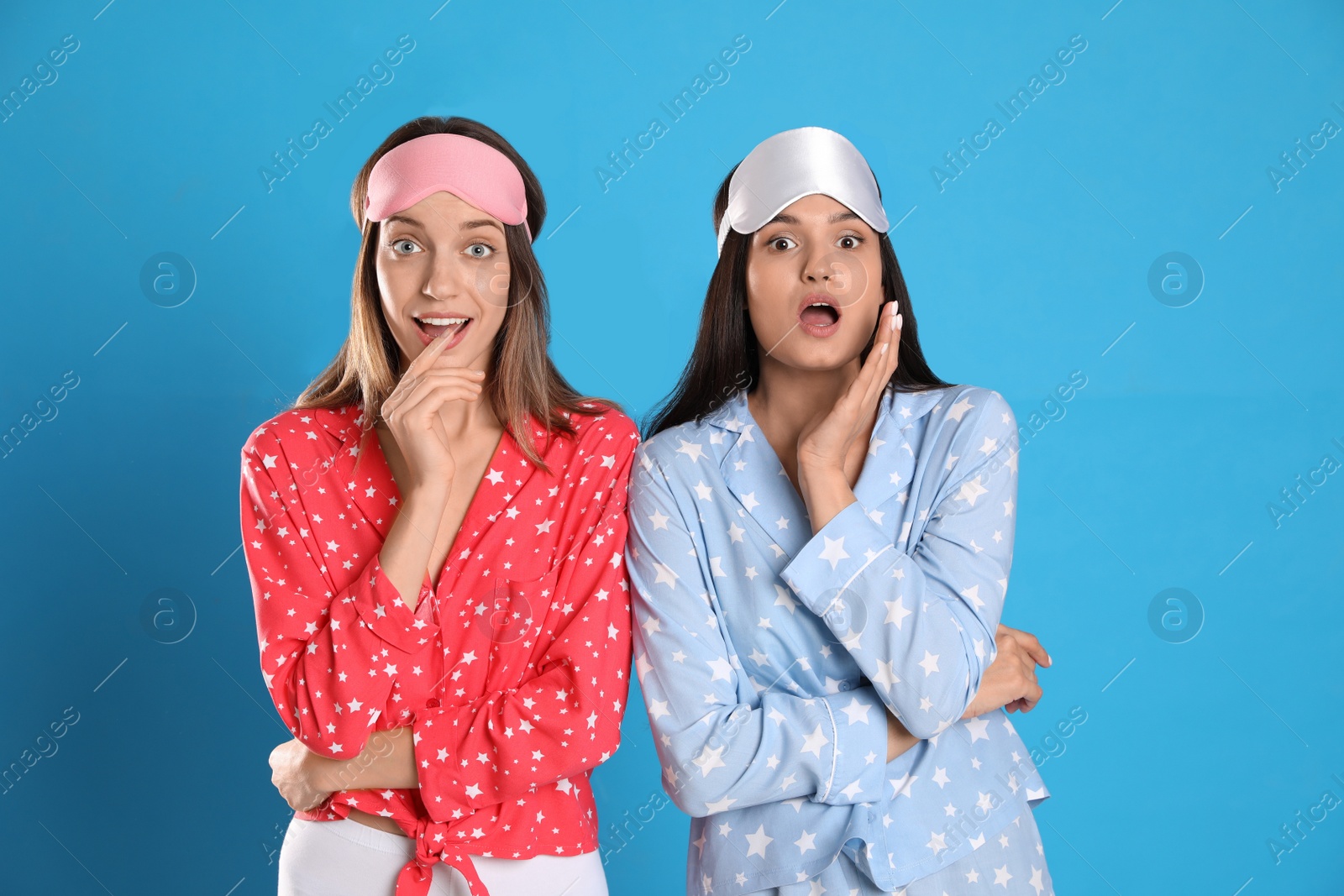 Photo of Beautiful women wearing sleeping masks on light blue background. Bedtime