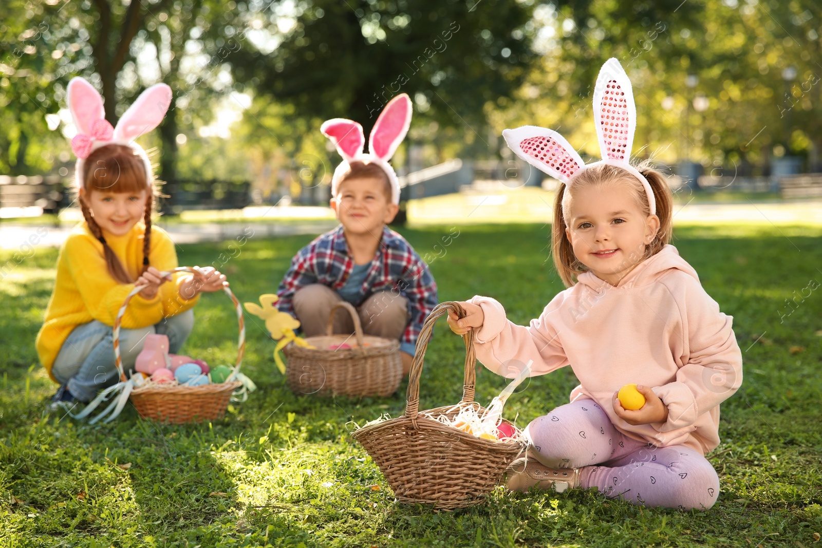 Photo of Cute little children hunting eggs in park. Easter tradition