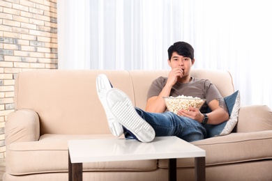 Young man with bowl of popcorn watching TV on sofa at home
