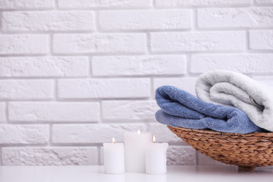 Photo of Basket with fresh towels and burning candles on table. Space for text