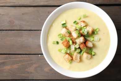 Photo of Tasty potato soup with croutons and green onion in bowl on wooden table, top view. Space for text