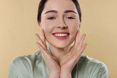 Young woman massaging her face on beige background