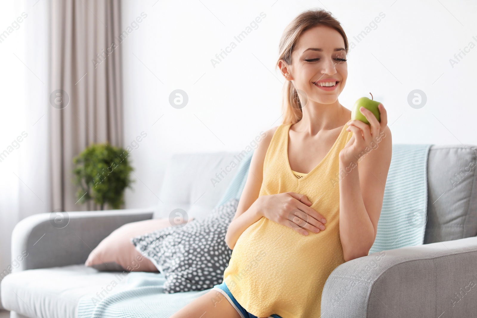 Photo of Young pregnant woman holding apple at home