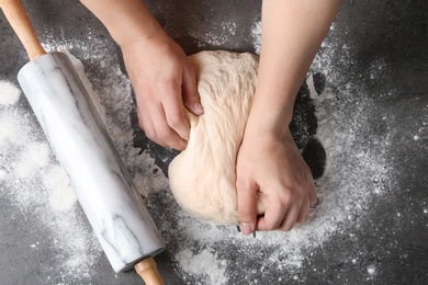 Photo of Female baker preparing bread dough at grey table, top view