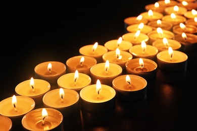 Photo of Wax candles burning on table in darkness, closeup