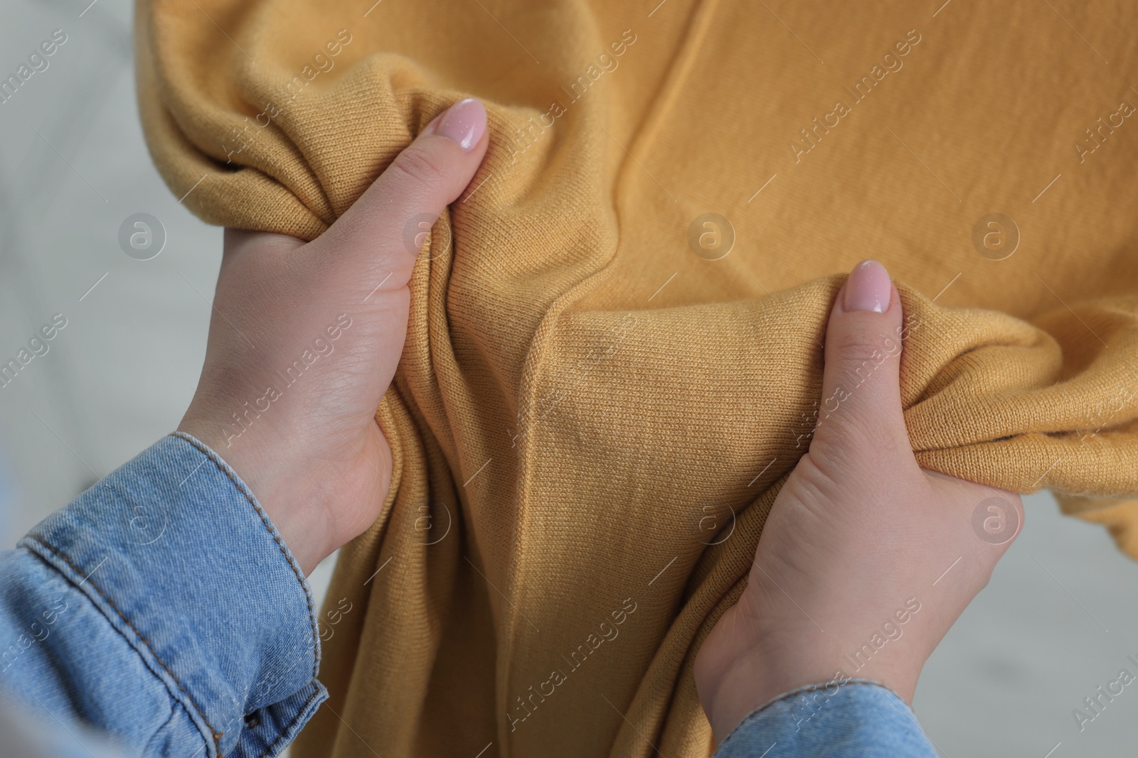 Photo of Woman touching clothes made of soft yellow fabric indoors, closeup