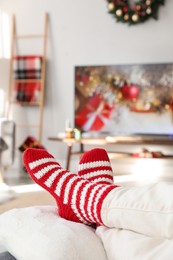 Photo of Woman in cute knitted socks watching TV at home, closeup