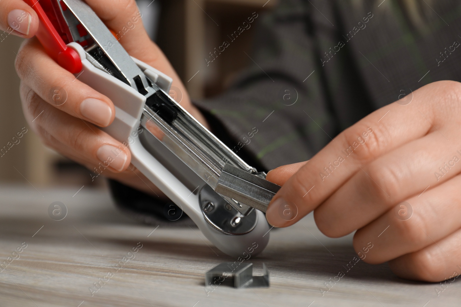 Photo of Woman putting metal staples into stapler at wooden table, closeup