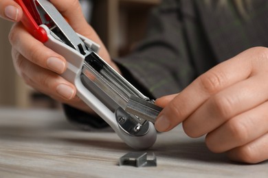 Photo of Woman putting metal staples into stapler at wooden table, closeup