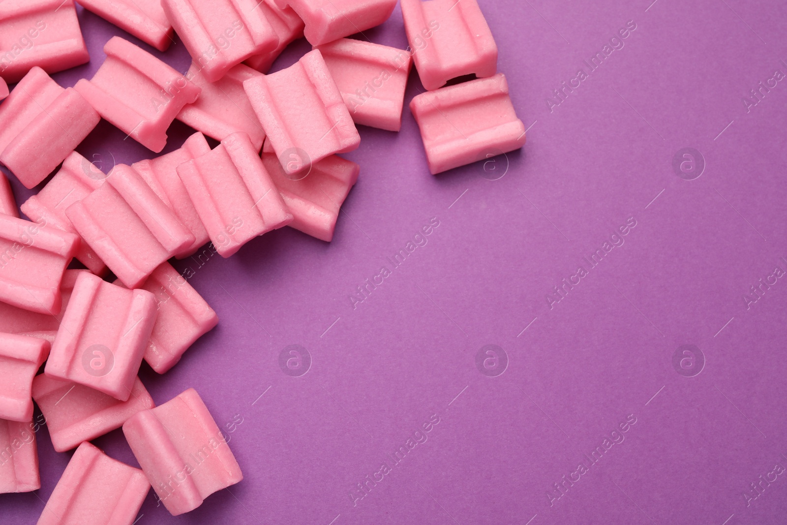 Photo of Tasty pink chewing gums on purple background, flat lay. Space for text