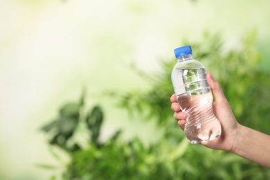 Photo of Woman holding bottle of water on blurred background. Space for text