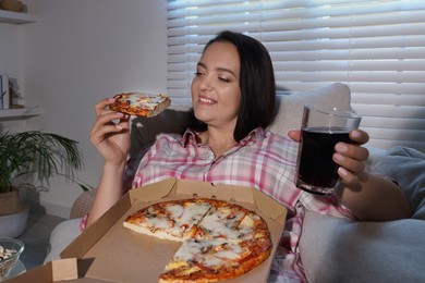 Photo of Happy overweight woman with pizza and cola on sofa at home